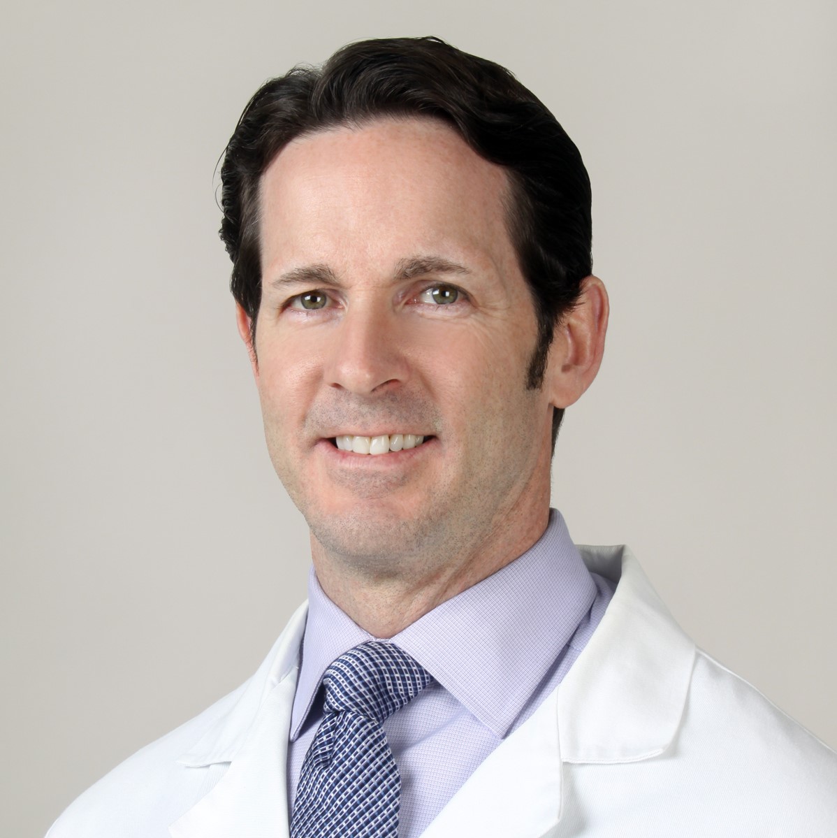 a man smiling wearing a lab coat against a grey background