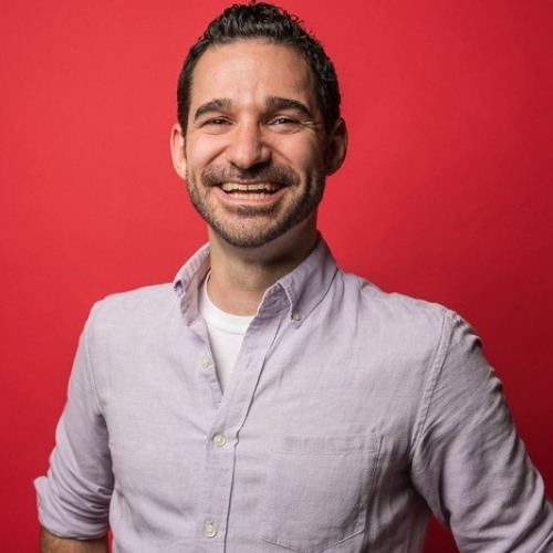 smiling man wearing a button up shirt against a red background