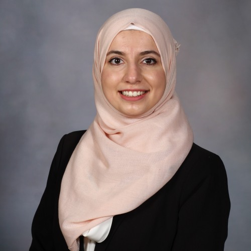 smiling woman wearing a light pink hijab and a black blazer