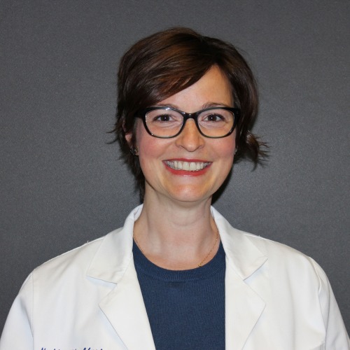 woman smiling wearing glasses and a lab coat against a dark blue background