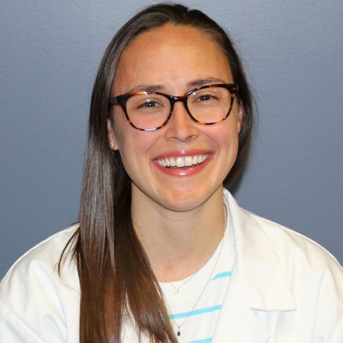 woman wearing glasses and a lab coat smiling against a blue background