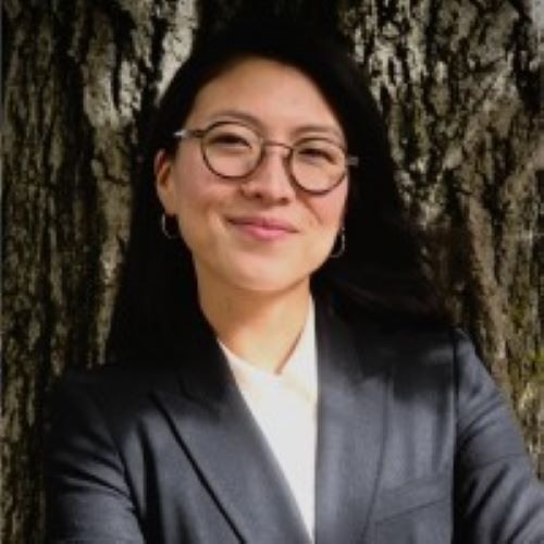 woman with glasses smiling against a tree