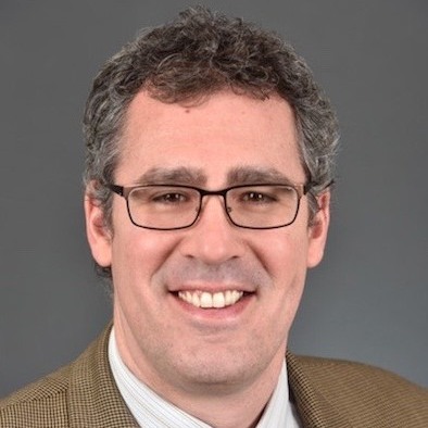 physician smiling wearing a tan blazer white button up and a black tie