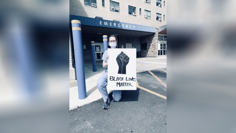 person kneeling outside emergency room with a sign that says Black Lives Matter