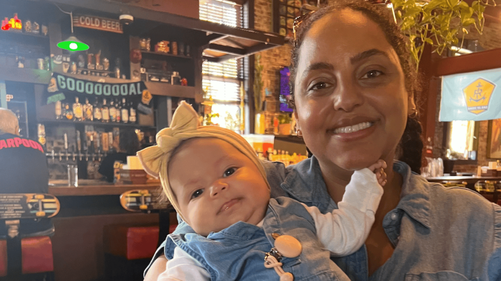 woman smiling wearing a blue dress and holding a smiling baby