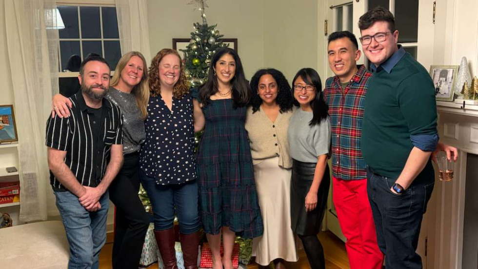 group of people standing in a living room in front of a Christmas tree