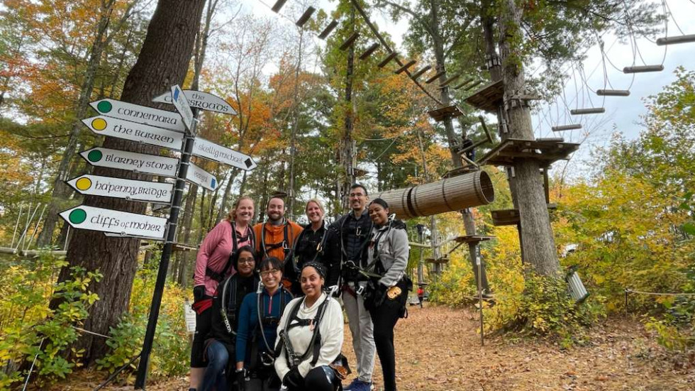group of people standing in the woods under an adventure course